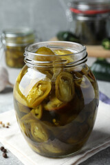 Glass jar with slices of pickled green jalapeno peppers on table