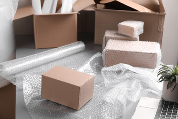 Table with laptop, boxes and bubble wrap in warehouse - obrazy, fototapety, plakaty
