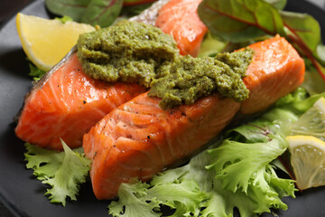 Tasty cooked salmon with pesto sauce on black plate, closeup