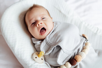 Cute caucasian blonde baby two months old lying in cocoon at home and yawning