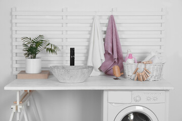 Laundry room interior with modern washing machine and stylish vessel sink on white wooden countertop