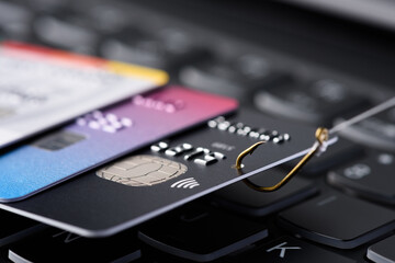 Credit card phishing scam concept. Credit card data theft, card hooked on fishing hook pulled from stack of other cards on keyboard. - 502826770