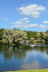 Fototapeta na wymiar vacationers ride a boat on a forest lake against the backdrop of a park and blue sky