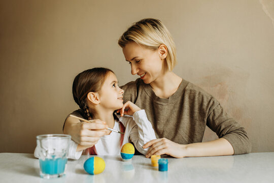 Portrait of a mother and daughter painting an egg in blue and yellow. Ukrainian family is preparing for Easter.