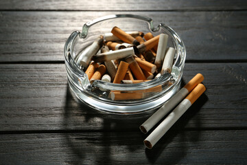 Glass ashtray with cigarette stubs on black wooden table
