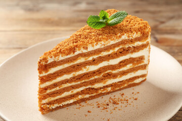 Slice of delicious layered honey cake with mint on plate, closeup