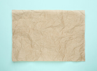 Sheet of crumpled brown baking paper on light blue background, top view