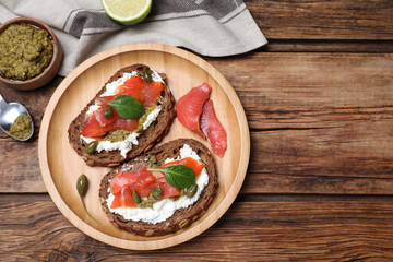 Delicious sandwiches with cream cheese, salmon, capers and pesto served on wooden table, flat lay. Space for text