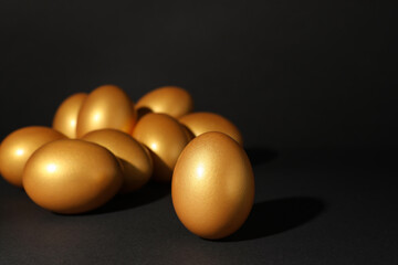 Many shiny golden eggs on black background. Space for text