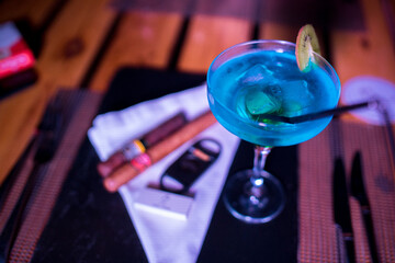 Closeup photo of many cigars on the table with a blue cocktail