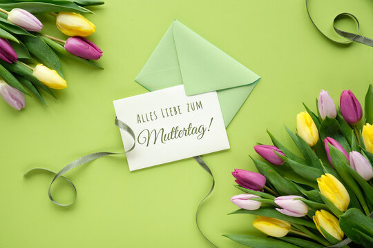 Alles Liebe zum Muttertag, that means in German All the love on Mother's day . Text on paper card. Flat lay with colorful tulips, flat lay on paper with ribbons.