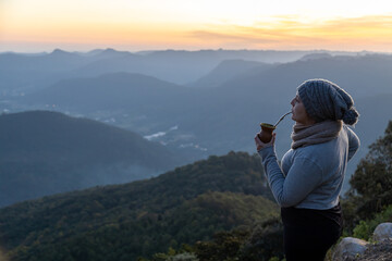 Fototapeta na wymiar Woman drinking yerba mate in the morning on the top of mountains, Rio Grande do Sul highlands, Brazil
