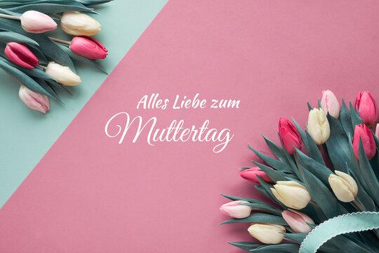 Alles Liebe zum Muttertag, that means in German All the love on Mother's day . Text on paper card. Flat lay with colorful tulips, flat lay on paper with ribbons.