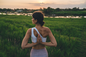 Back view of calm female yogi practicing namaste breathing in yoga pose seeking inner peace on leisure, relaxed fit girl in sportswear keeping body shape in tonus enjoying hatha style of workout