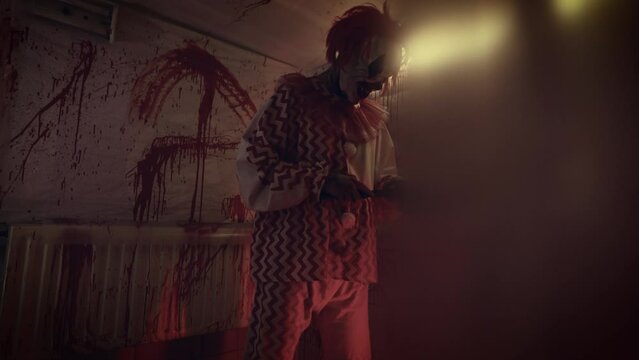 Crazy maniac in a clown costume in his bloody lair. Terrible image from nightmares.