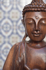 Fototapeta na wymiar Wooden statue of Buddha in front of a tiled backdrop 