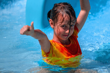 Young girl on water slide at water park raising hands and raising thumbs up. Summer water park...