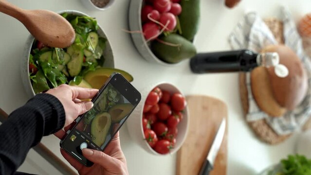 Closeup of female hands holding smartphone and taking pictures for social media in kitchen, cooking dietary meal from fresh vegetables in bowl. healthy eating concept. Vertical shoot. 4k footage
