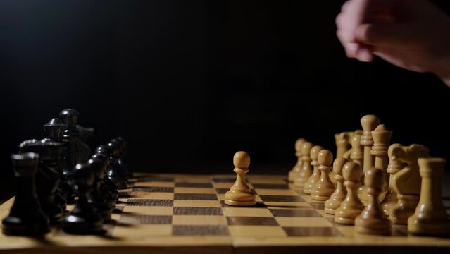 Opening Queen Gambit of the chess game with the move of the white pawn d2-d4, black background. A man hand with a chess piece in a board game.