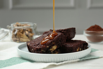 Pouring caramel sauce onto delicious chocolate brownies with nuts on white table