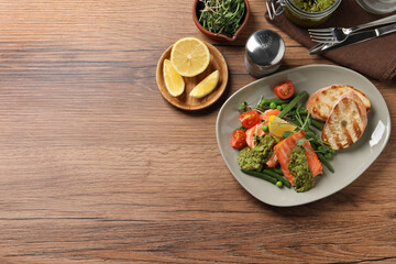 Tasty cooked salmon with pesto sauce served on wooden table, flat lay. Space for text