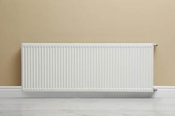 Modern radiator on beige wall indoors. Central heating system