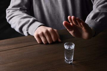 Man refusing to drink vodka at wooden table, closeup. Alcohol addiction