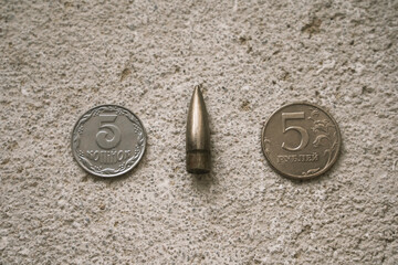 Two coins, Russian and Ukrainian, on the concrete floor with a bullet between them. Finance and the army.