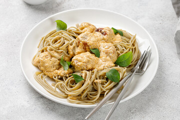 Whole grain pasta with meatballs with cream sauce and greens on white plate, grey background