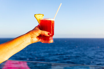 Frau mit Cocktail in der Hand an der Reling eines Schiffes, blauer Ozean und Himmel im Hintergrund.