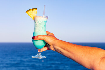 Frau mit Cocktail in der Hand an der Reling eines Schiffes, blauer Ozean und Himmel im Hintergrund.