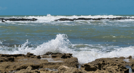Linda praia com muitas pedras sendo banhadas pelas ondas, sob um lindo céu azul, localizada em Cabrália na região de Porto Seguro, Bahia, Brasil.