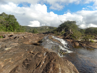Linda queda D'água entre pedras, com muita vegetação em volta e céu azul, localizada na região rural de Três Barras, município do Serro, Minas Gerais, Brasil.