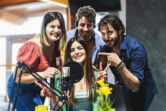A team of four presenters greets the audience of their live streaming vlog podcast via the internet - a group of content creator influencers speak into the microphone during a live broadcast - 