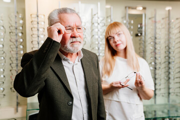 an elderly man with an ophthalmologist chooses glasses in the optics salon.