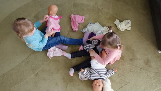 Close up happy adorable little preschool kids girls plays enjoy game with dolls sitting on a rug in the living room,