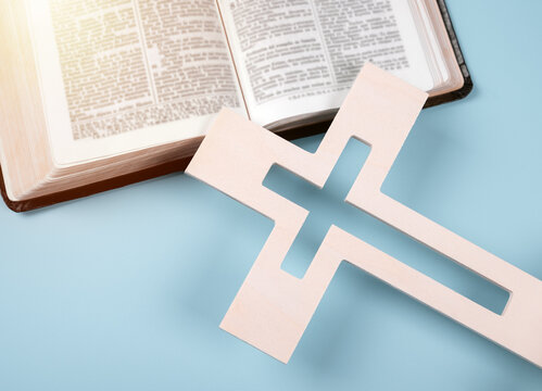 Closeup Of Wooden Christian Cross On Open Holy Bible On Blue Background.