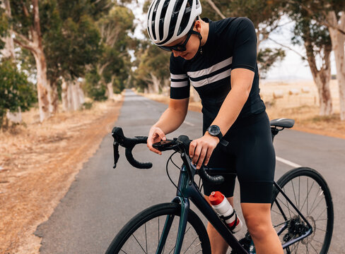 Professional Woman Cyclist Checking On Board Computer On Her Road Bike On Empty Road