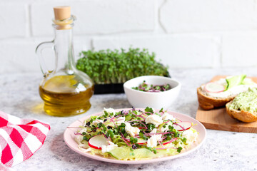 Delicious homemade salad of cabbage, cucumbers, radishes, cream cheese and microgreens on the kitchen table. Healthy food. Selective focus