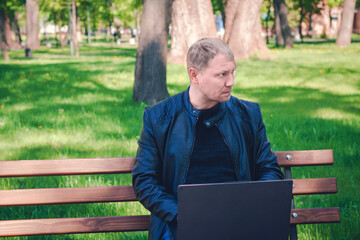 Fototapeta premium Technology, communication, education, copy space. Remote work concept, Man connected on internet outside the house. Concentrated man working on laptop in pleasant atmosphere in park