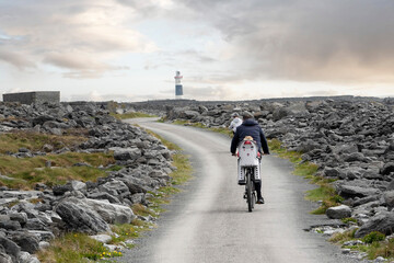 Family with children cycling on small narrow country road in rough stone terrain to a lighthouse....