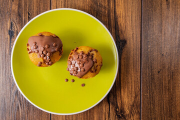 Two chocolate chip muffins on a yellow plate and wooden table . Copy space. Premium quality bakery product.