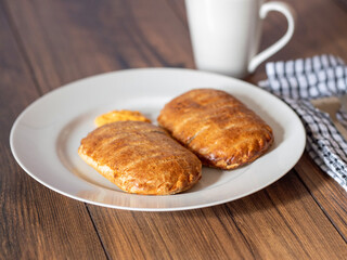 Serving of two ham and cheese pies on a white plate on wooden table. Simple food concept. Pastry product for lunch.