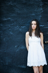 Fototapeta na wymiar A beautiful teen brunette girl with a serious look leaning against a wall in thought