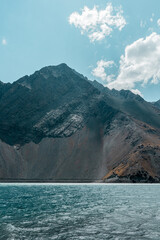 Vertical shot of turquoise water in the Embalse del Yeso reservoir with colored mountains in the background, Chile.