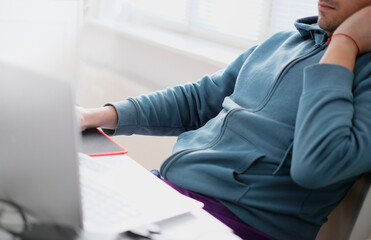 A man in a turquoise sweater in a bright office while working at a computer close-up. Work illustration