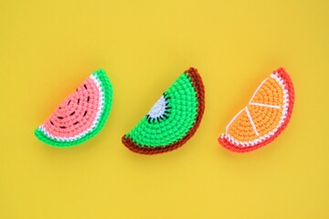 Colourful crochet handmade slices of watermelon, kiwi and orange on yellow background. Summer vacation creative tropical bright minimalistic food concept. Flatlay, top view holiday composition.