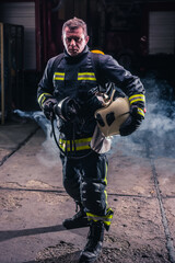 Obraz premium Portrait of young fireman standing and holding a chainsaw in the middle of the chainsaw's smoke .