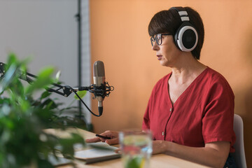 Mature woman making podcast recording for her online show. Attractive business woman using...