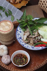 Thai food "Spicy Grilled Pork Salad" served on a wooden table with grilled chicken.
